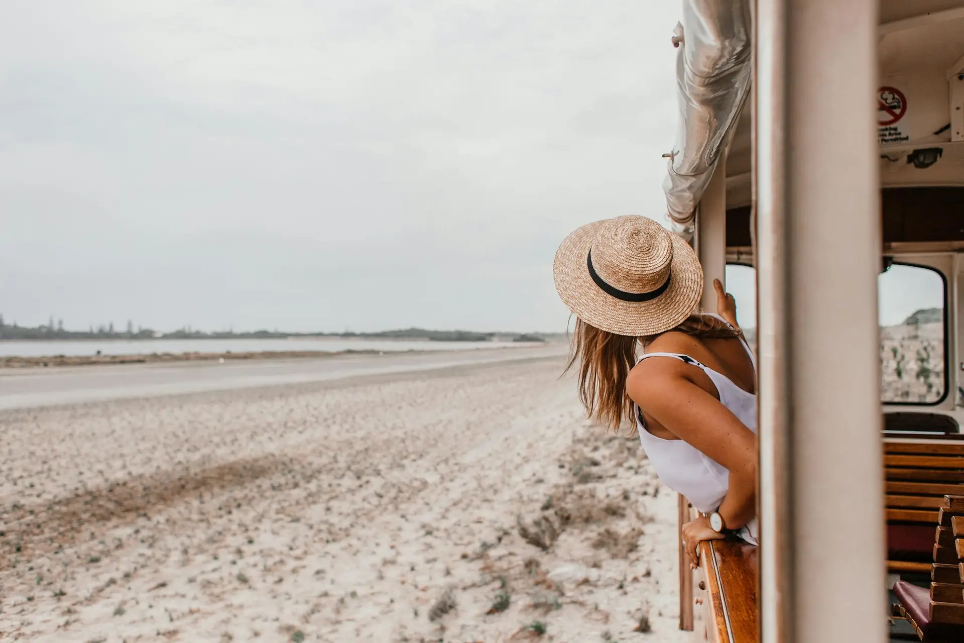 Solo Travel Safety Tips: Woman in straw hat leans out of a train window, enjoying a beachside journey.