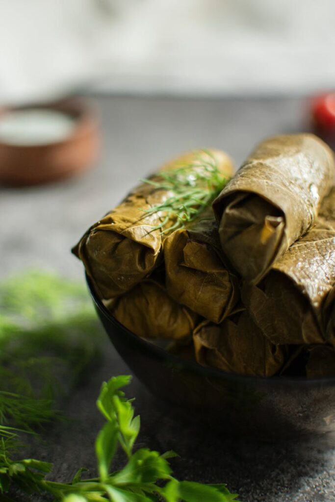 Close-up of freshly prepared stuffed grape leaves in a bowl, garnished with herbs.