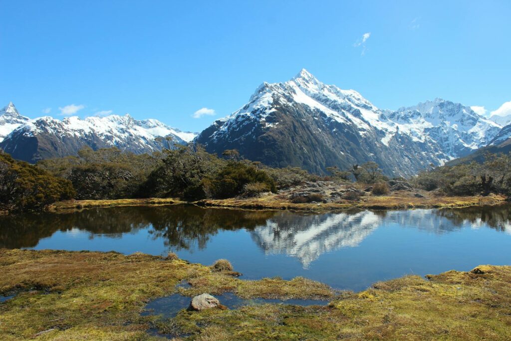 Scenic Road Trips in New Zealand: Breathtaking view of snowcapped mountains reflected in a serene lake.