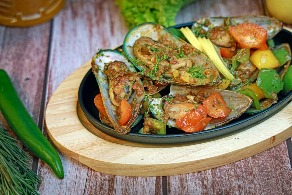 Scenic Road Trips in New Zealand: A vibrant seafood dish featuring green mussels and vegetables on a wooden plate.