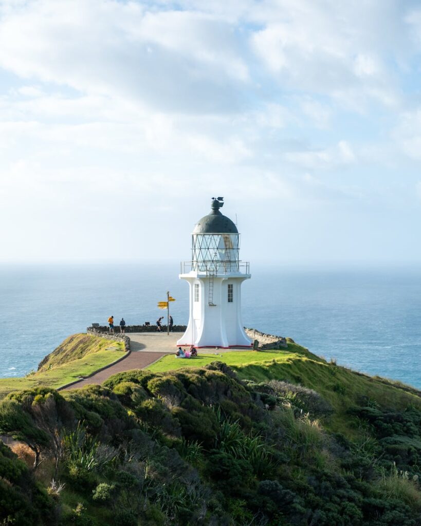 Scenic Road Trips in New Zealand: Scenic view of Cape Reinga Lighthouse in Northland, New Zealand, perched on a cliff by the sea.