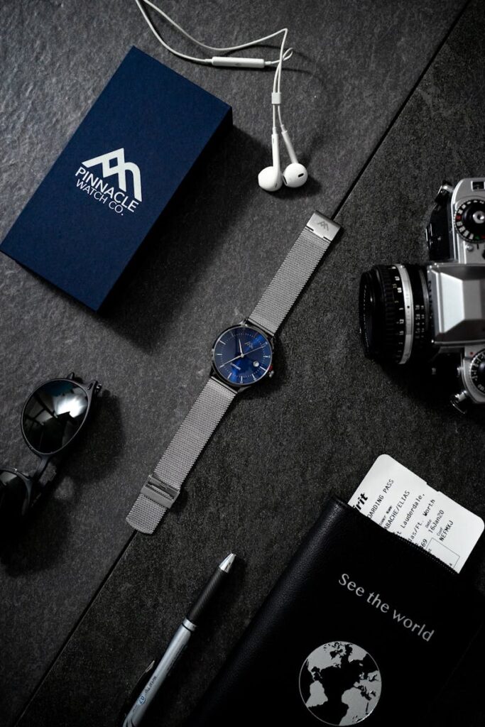 Packing Light for Travel: Stylish flat lay of watch, camera, passport, and travel items on dark surface.