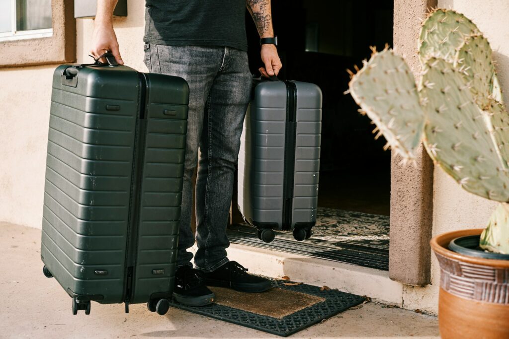 Packing Light for Travel: man in black denim jeans and black leather shoes standing beside black luggage bag