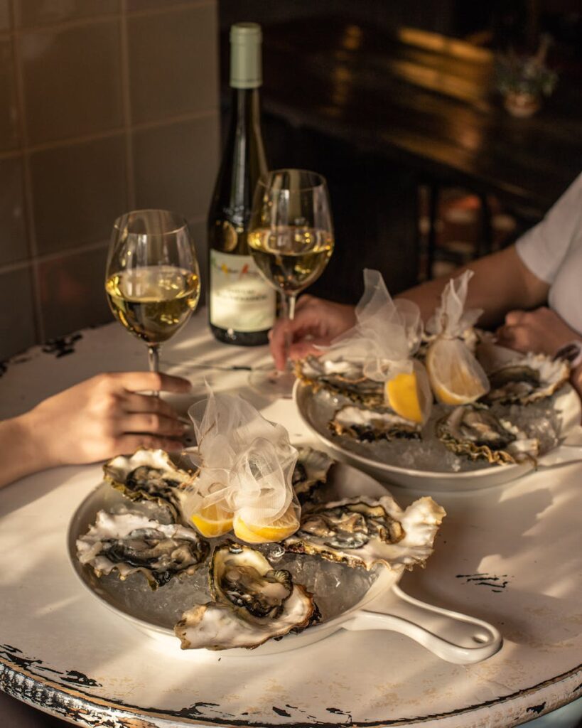 Australia and New Zealand Food Guide: Crop romantic couple having dinner in restaurant drinking white wine and eating oysters with lemon juice