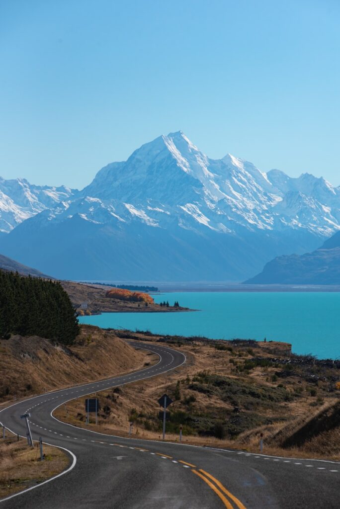 Scenic Road Trips in New Zealand: snow covered mountain near body of water during daytime