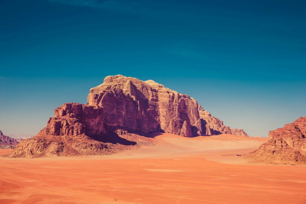 Best deserts to visit in the middle east: Wadi Rum, brown rock formation surrounded by sand dunes