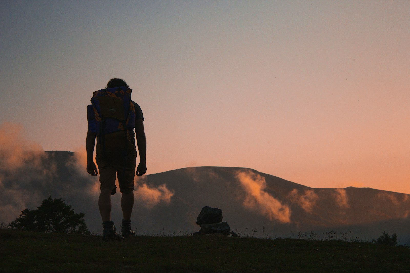 budget travel in Africa: silhouette of man walking along field leading to mountain